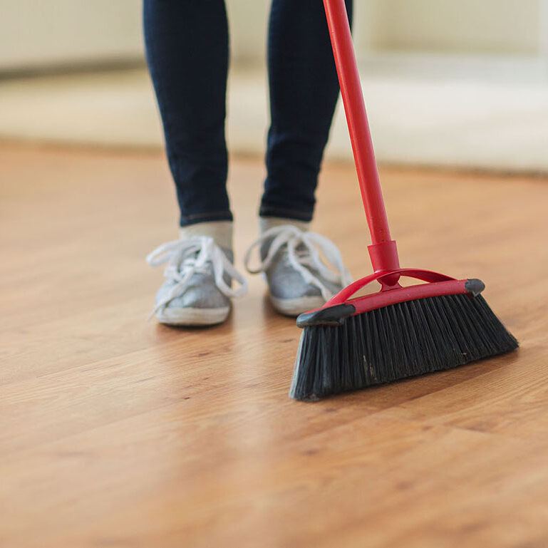 people, housework, cleaning and housekeeping concept - close up of woman legs with broom sweeping floor at home